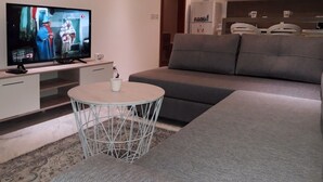 A modern living room with a flat-screen TV, a grey sofa, a small round table with a white mug, and a patterned rug.