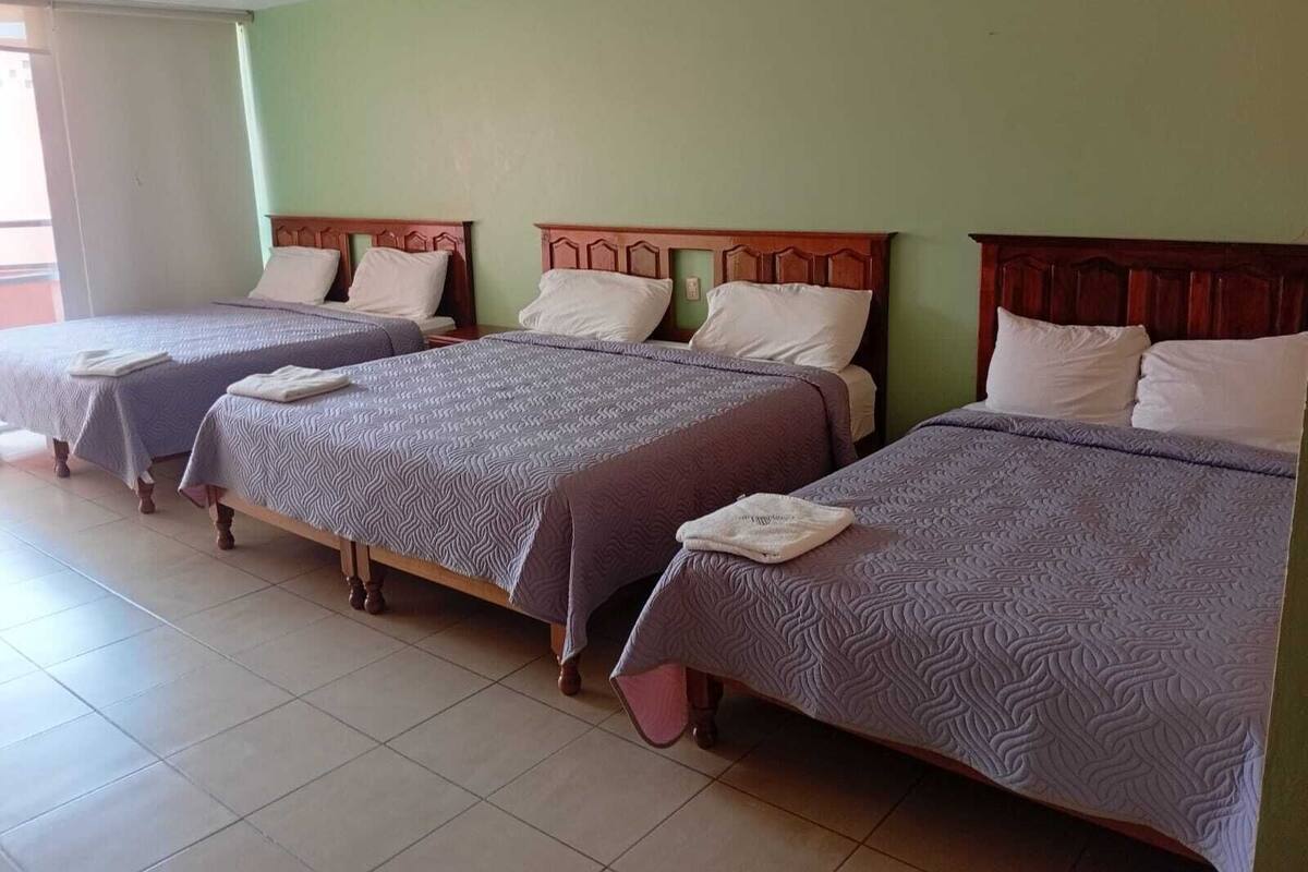 A hotel room with three single beds, each with a wooden headboard and a patterned bedspread.