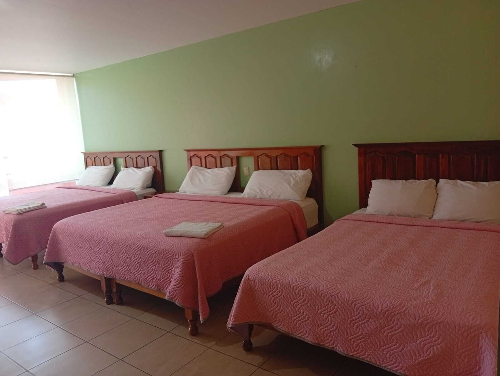 A hotel room with three beds, each with a wooden headboard and pink bedding.