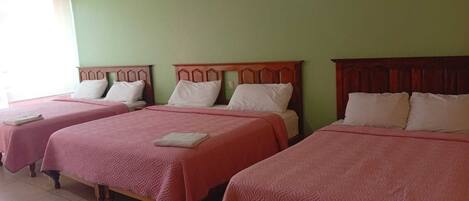A hotel room with three beds, each with a wooden headboard and pink bedding.