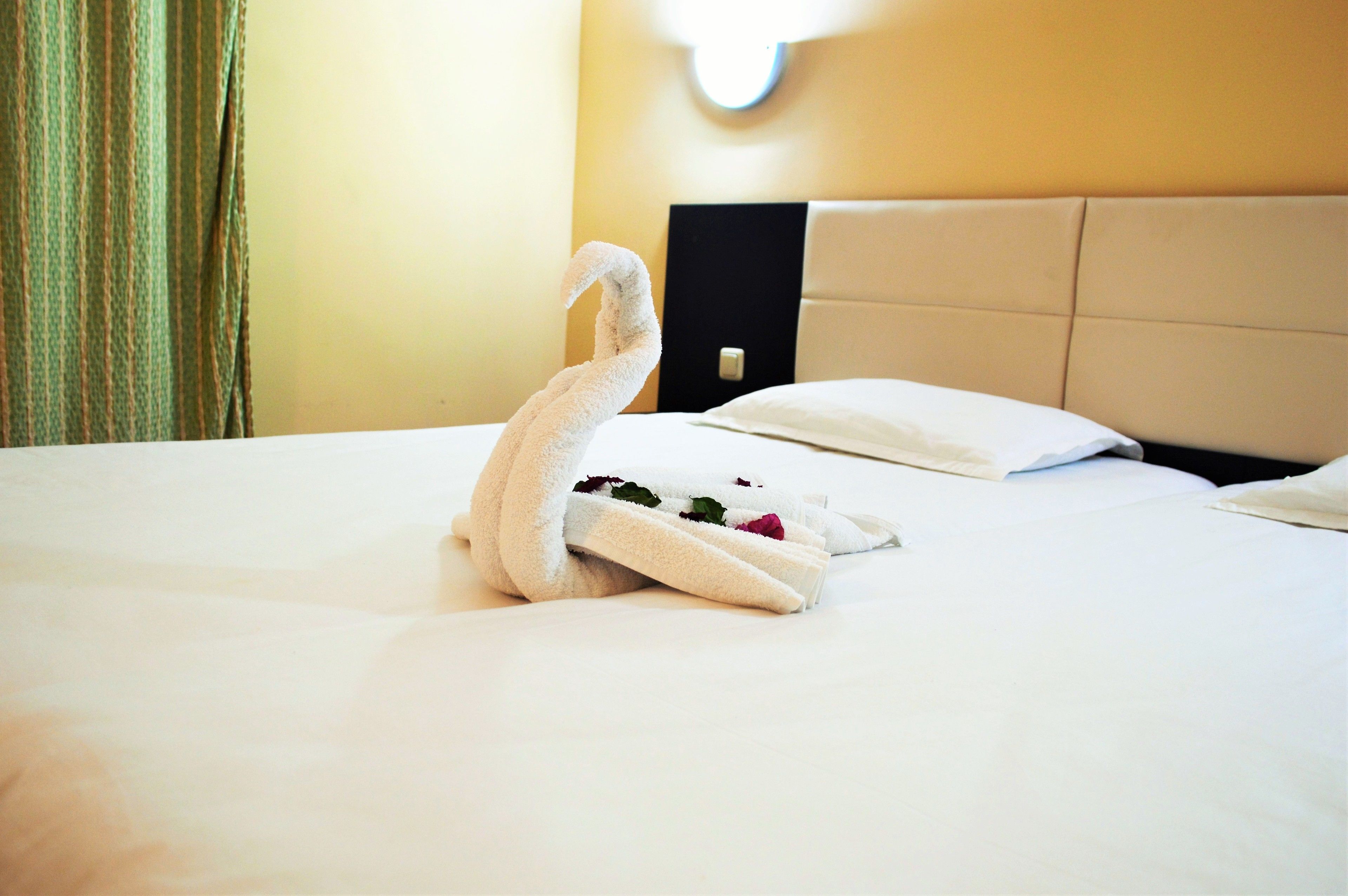A neatly made swan-shaped towel on a bed with white sheets and a beige headboard.