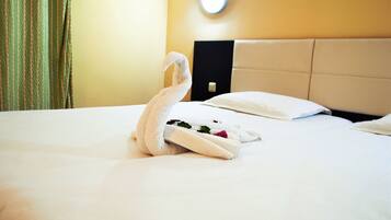 A neatly made swan-shaped towel on a bed with white sheets and a beige headboard.