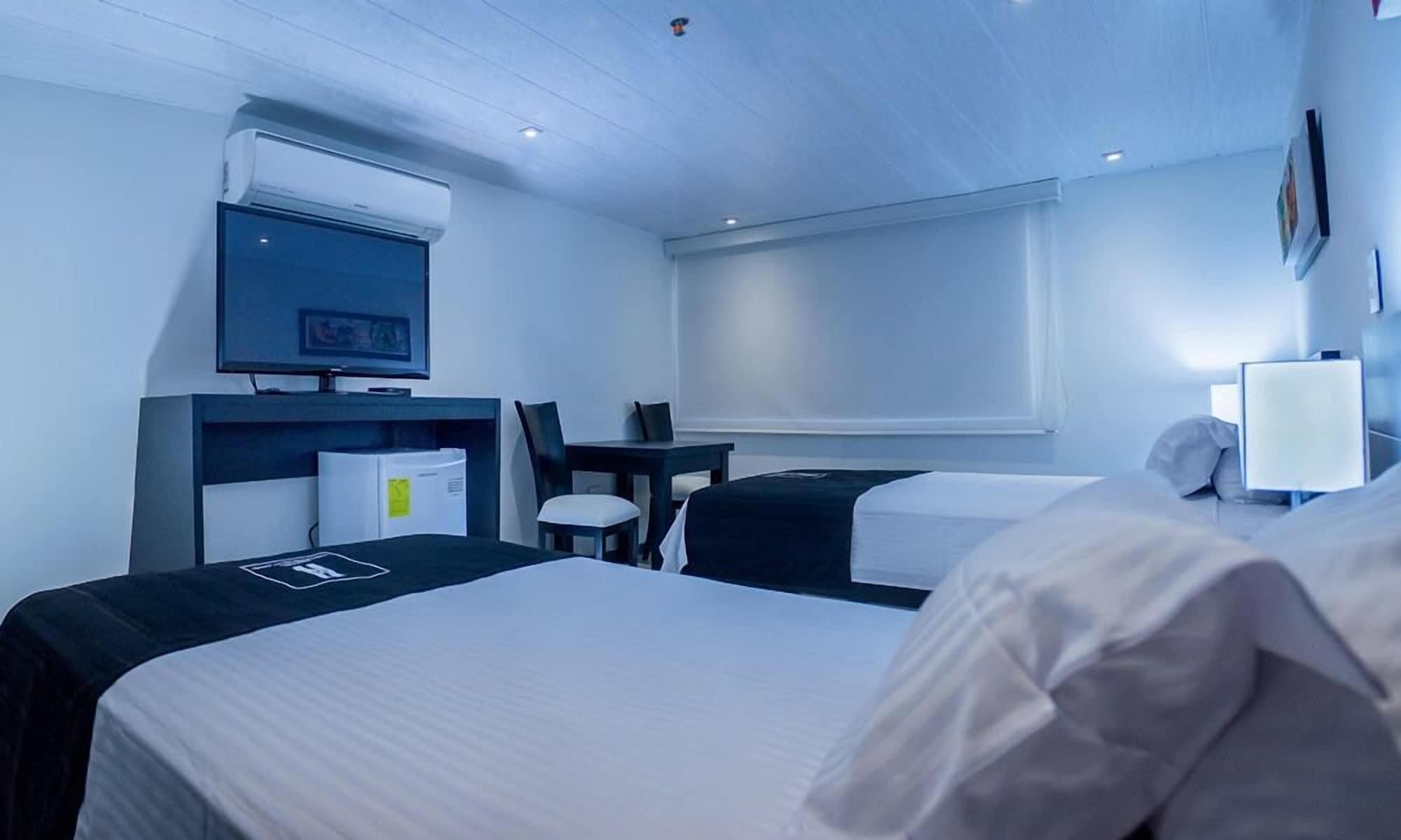 A hotel room with a bed, a desk, a chair, a TV, and a window.