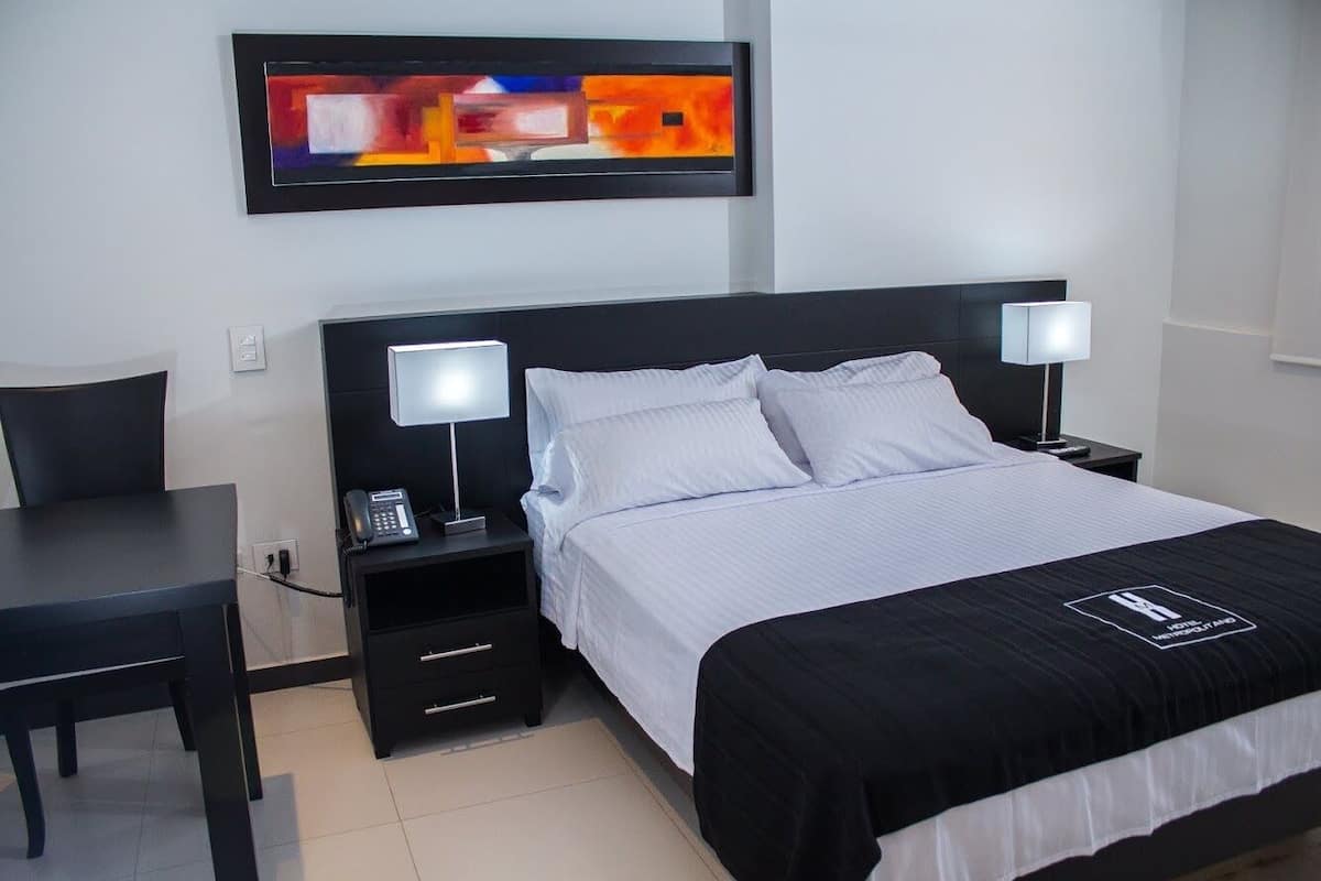 A hotel room with a bed, two bedside tables with lamps, a desk, and a painting on the wall.