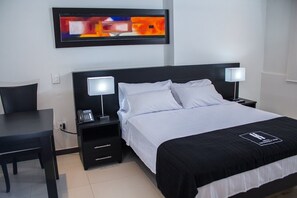 A hotel room with a bed, two bedside tables with lamps, a desk, and a painting on the wall. - Hotel Metropolitano (Neiva)