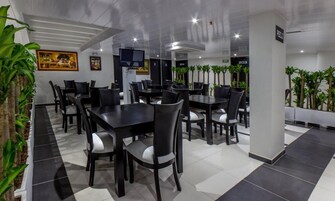 Un comedor moderno con mesas y sillas negras, plantas en macetas y obras de arte en las paredes.