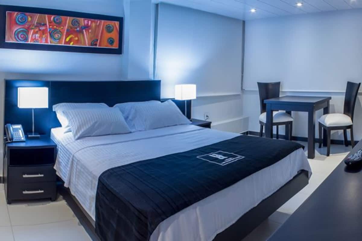 A modern hotel room with a large bed, bedside tables, a desk, and a chair.