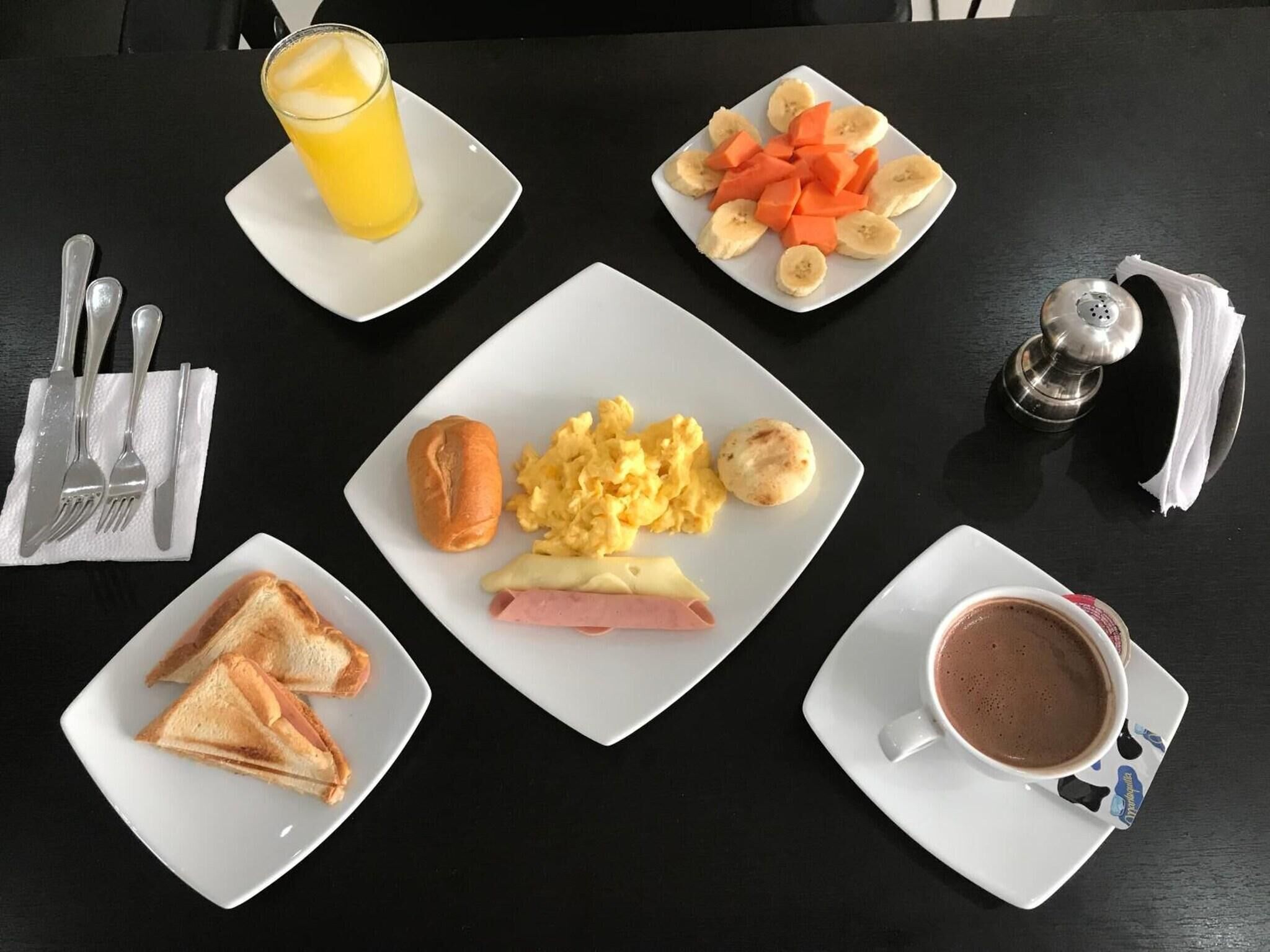 A breakfast setting with plates of toast, scrambled eggs, ham, and fruit, along with a glass of orange juice and a cup of coffee.