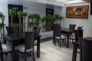Un comedor moderno con mesas y sillas negras, plantas en macetas y un cuadro en la pared.