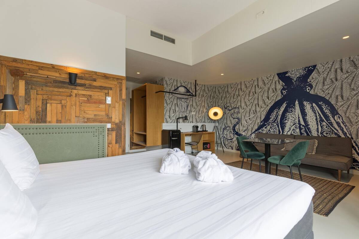A hotel room with a large bed, a desk with a chair, a sofa, and a wall with a large abstract design.