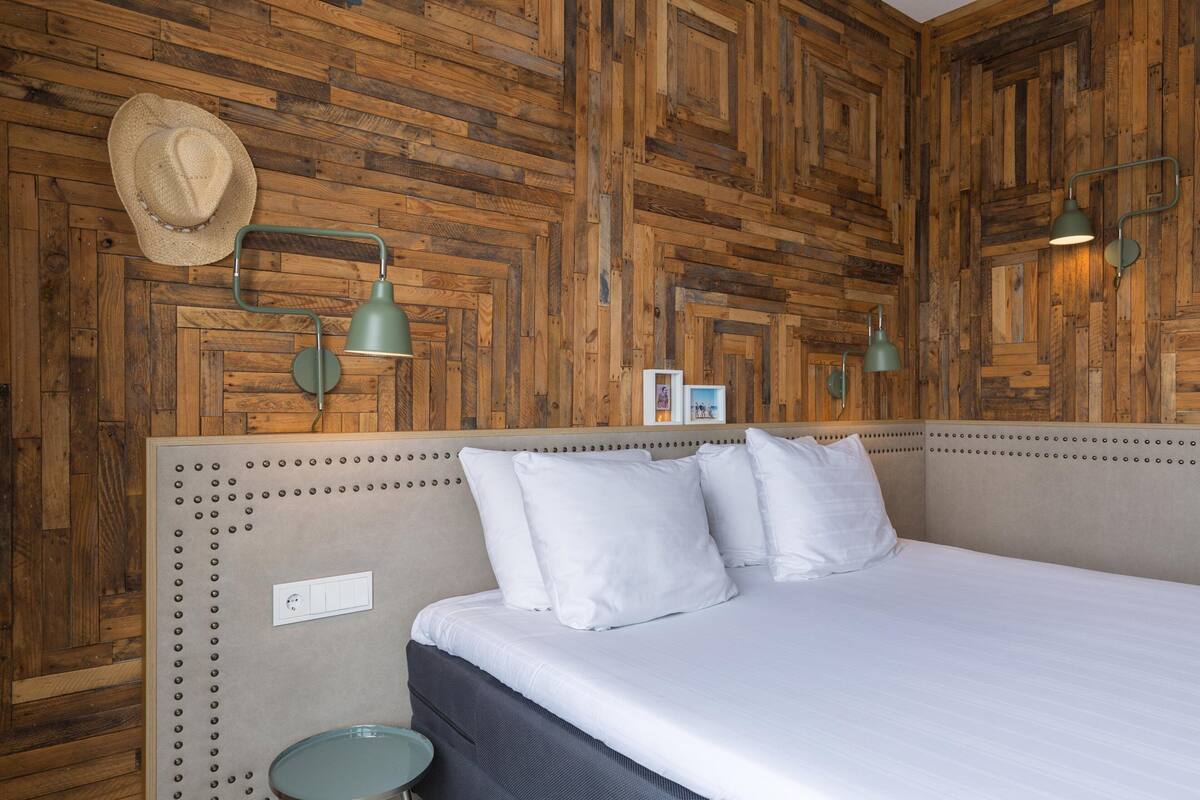 A room with a wooden wall panel, a bed with white bedding, and two wall-mounted lamps.