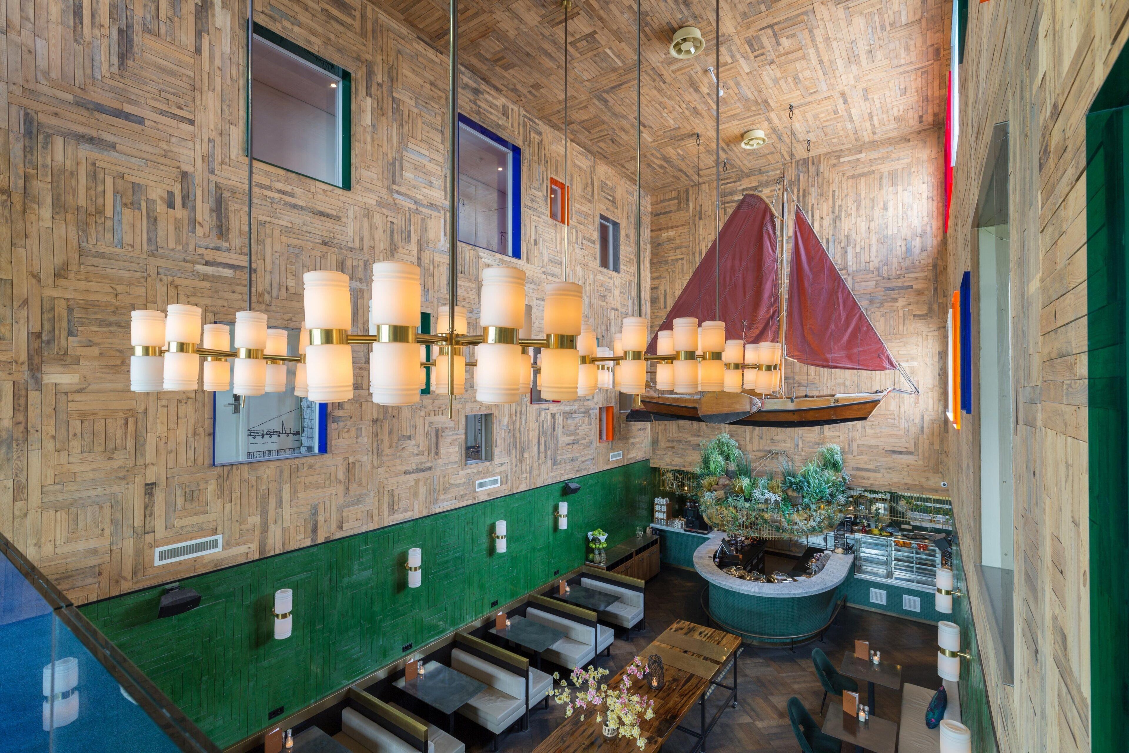 A spacious lobby with a wooden ceiling, a large sailboat decoration, and a seating area with a green wall and a plant.
