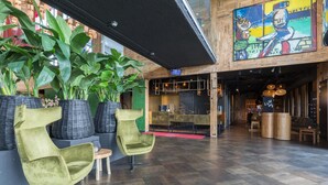 Un vestíbulo con diseño moderno, que presenta una planta grande, dos sillas verdes, piso de madera y un mural colorido en la pared.
