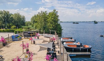 Um píer à beira do lago com barcos, uma área de estar com assentos e uma placa com a inscrição 'The Harbour Club'.