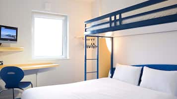 Una habitación de hotel con una cama litera, un escritorio con computadora, una silla y una ventana.