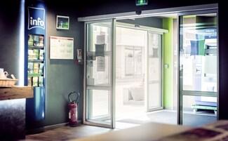 Un hall de hotel con mostrador de recepción, extintor y puerta de vidrio que da al área de recepción.