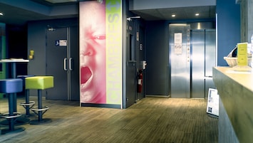 Un moderno vestíbulo de hotel con una recepción, una cabina fotográfica digital y una zona de estar con taburetes.