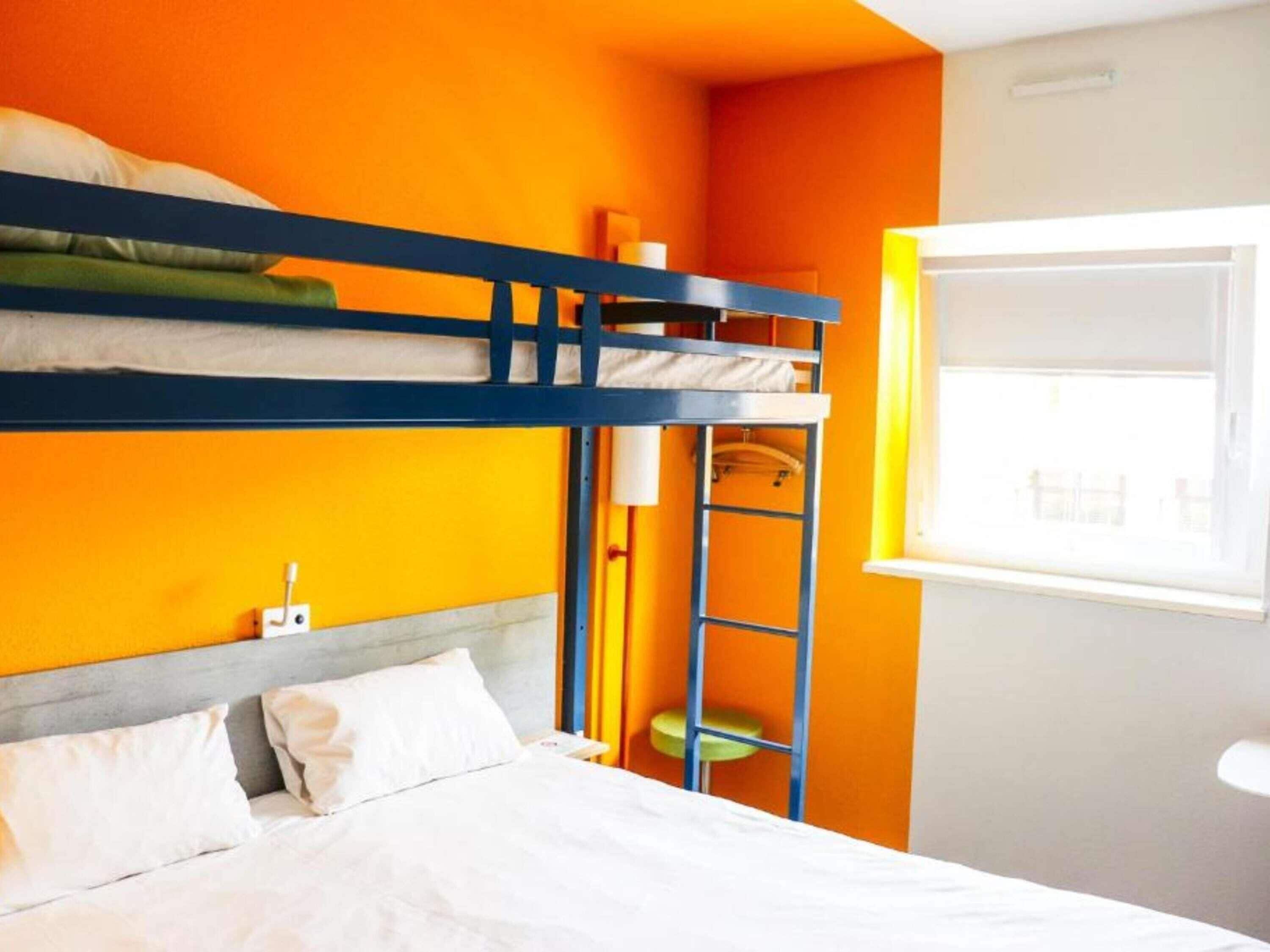 A bunk bed room with a window, a chair, and a small table.