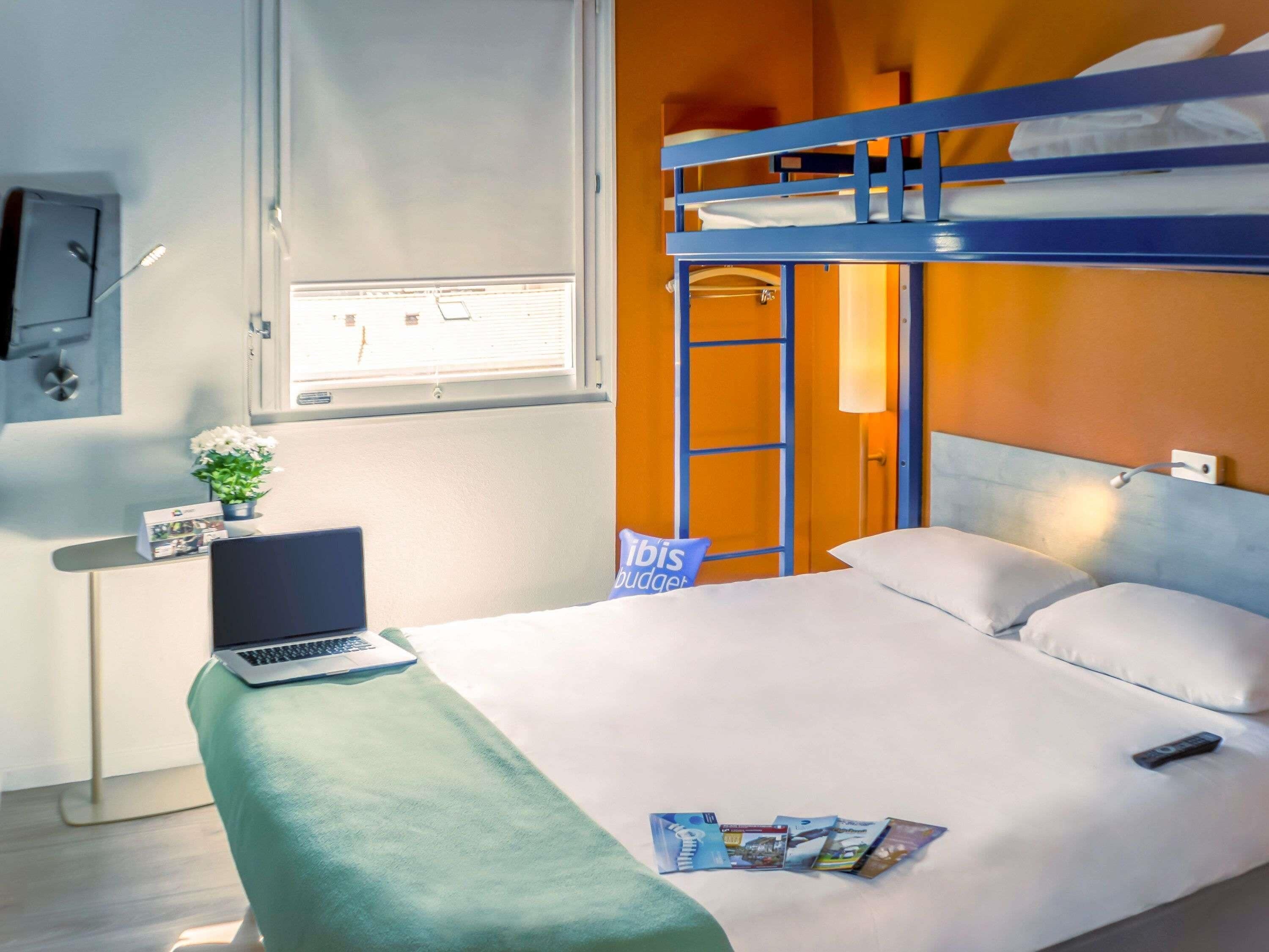 Una habitación de hotel con literas, un escritorio con una computadora portátil, una planta pequeña y un cartel que dice "Ribis Budjet".