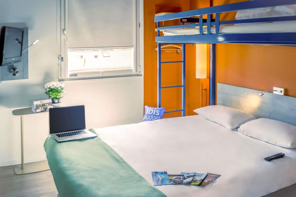 Una habitación de hotel con literas, un escritorio con una computadora portátil, una planta pequeña y un cartel que dice "Ribis Budjet".