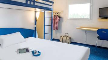 Una habitación de hotel con literas, un escritorio, una silla, un televisor y una ventana.