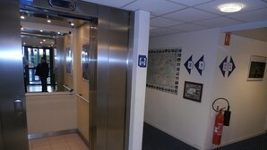 Un ascensor con pantalla digital, un extintor y una pared con señales direccionales y un mapa.