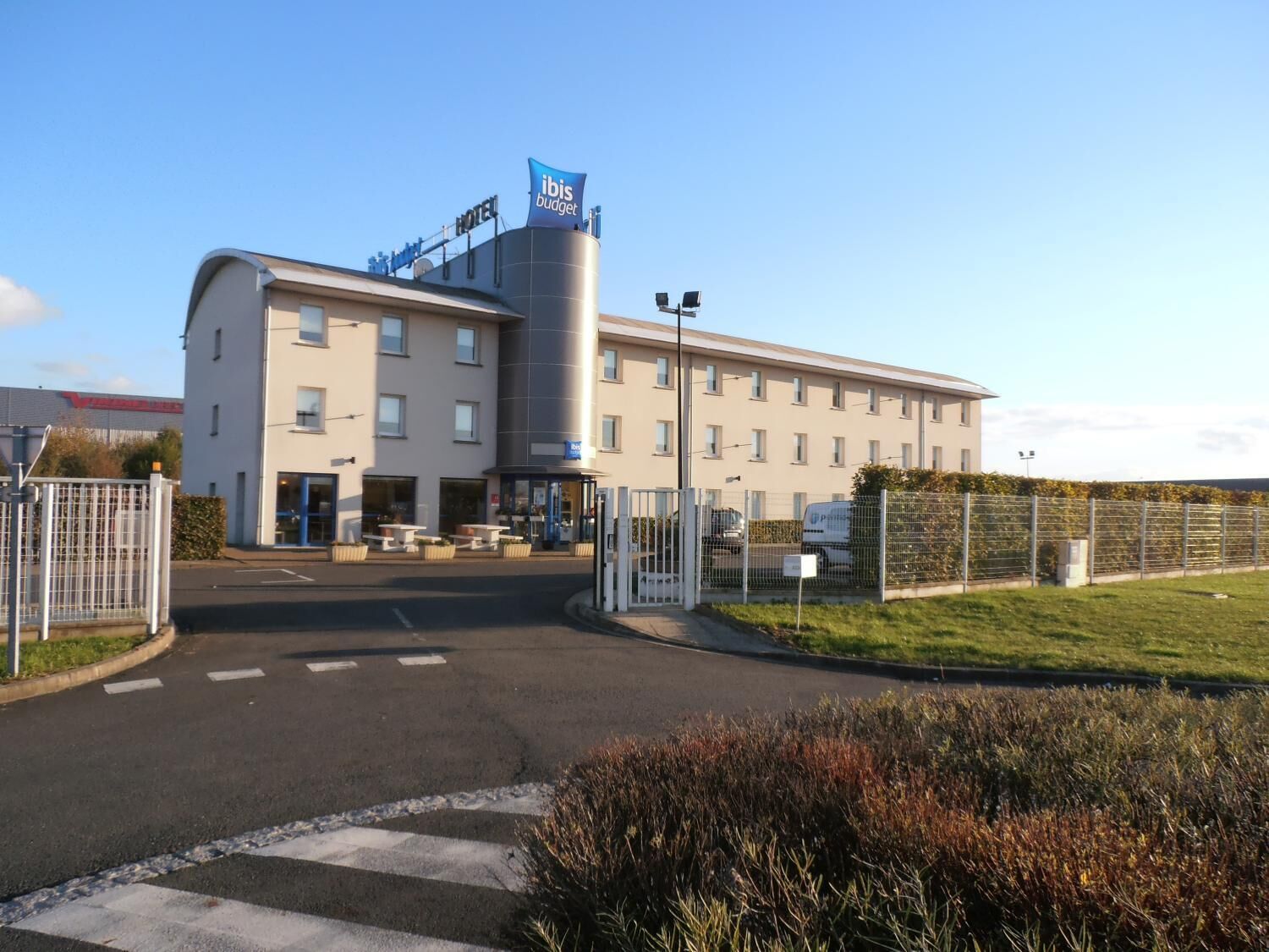 A modern hotel with a prominent 'ibis budget' sign, a covered outdoor seating area, and a gated entrance.