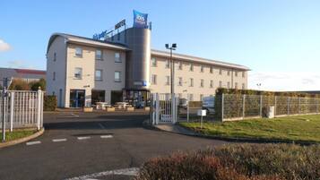 A modern hotel with a prominent 'ibis budget' sign, a covered outdoor seating area, and a gated entrance.