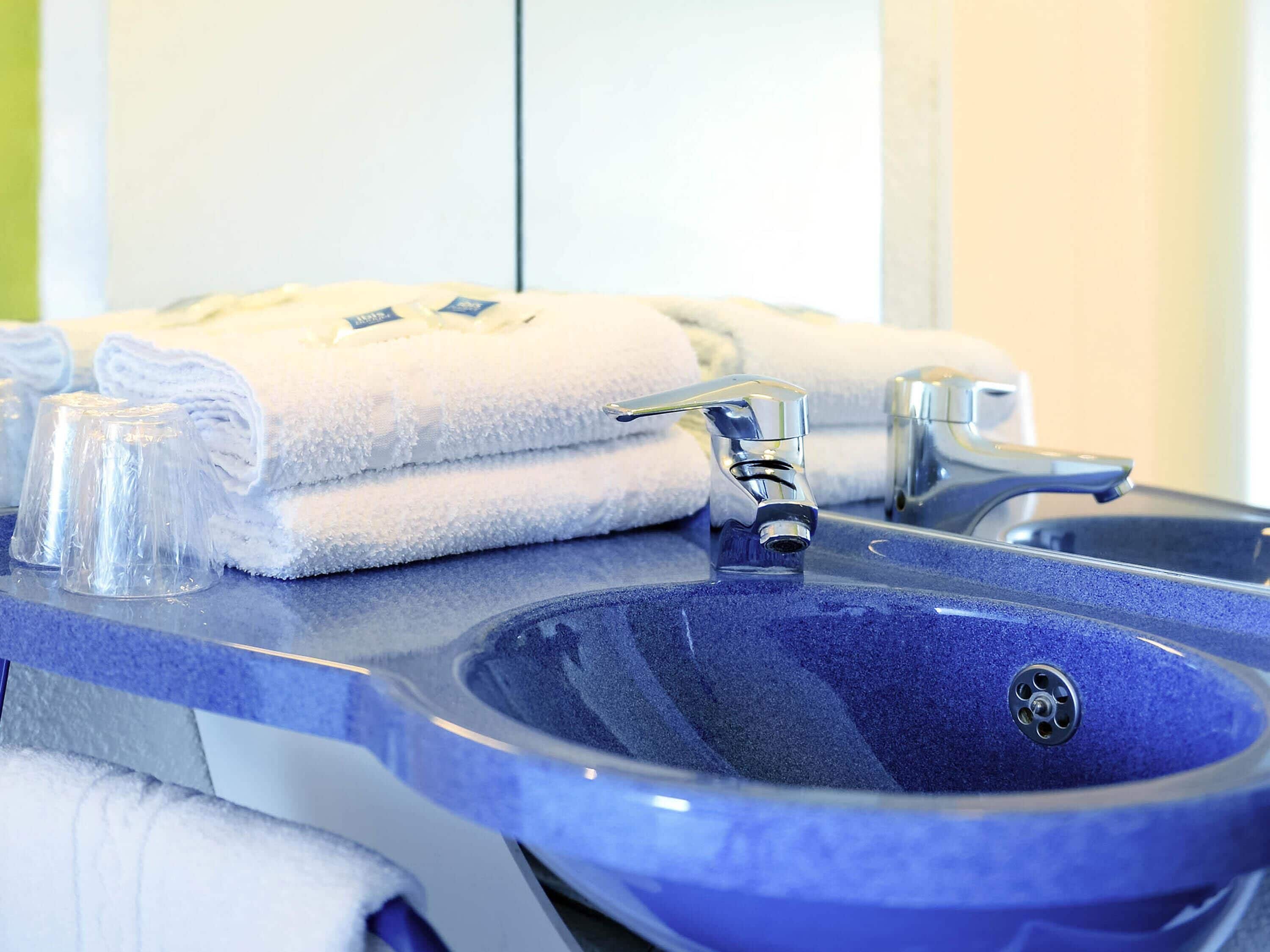 A bathroom with a blue sink, two faucets, and stacked white towels.