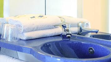 A bathroom with a blue sink, two faucets, and stacked white towels.