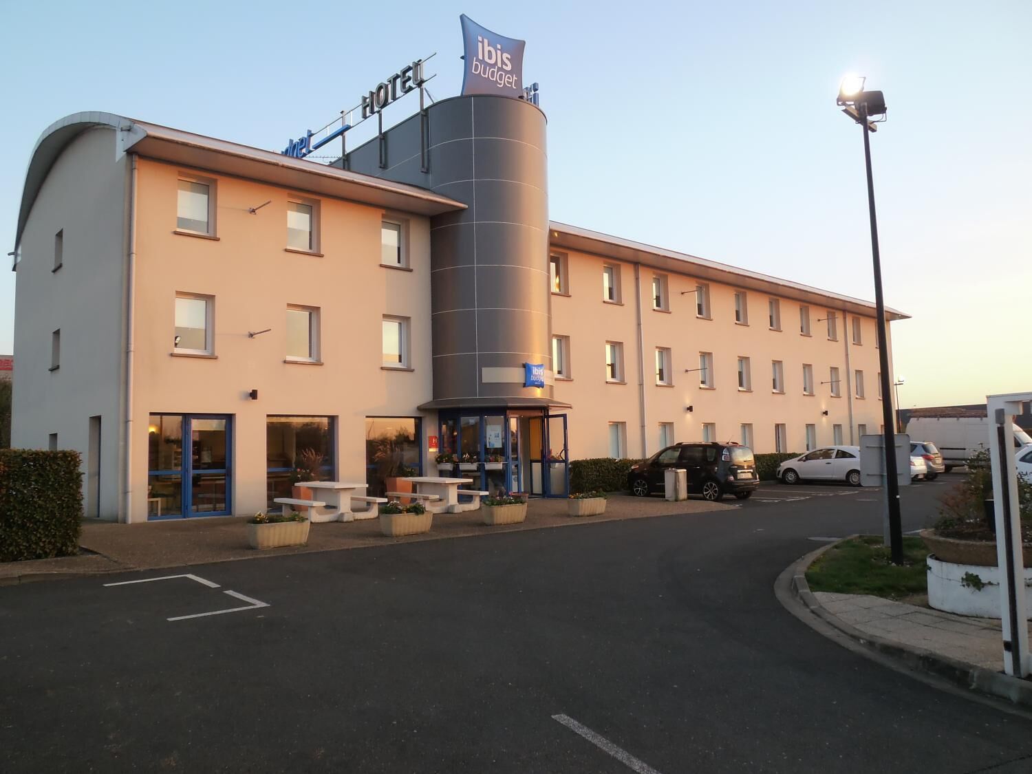 Een modern hotel met een gebogen gevel, een terras en een opvallende cilindervormige constructie.