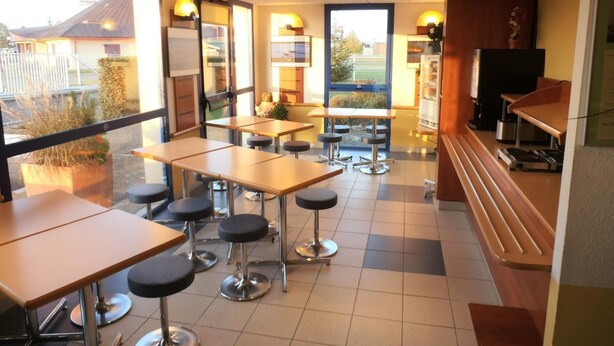 Un restaurante con varias mesas y taburetes, ventanas amplias y vistas al exterior.