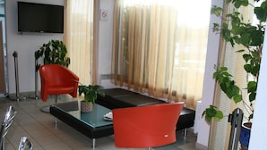Una sala de estar moderna con una mesa de centro de vidrio, dos sillas rojas, un sofá negro y un televisor montado en la pared.