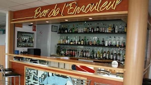 Zona de bar con un letrero de neón que dice "Bar de l'Emouleur", con una variedad de botellas de licor en estantes y varios taburetes de bar.