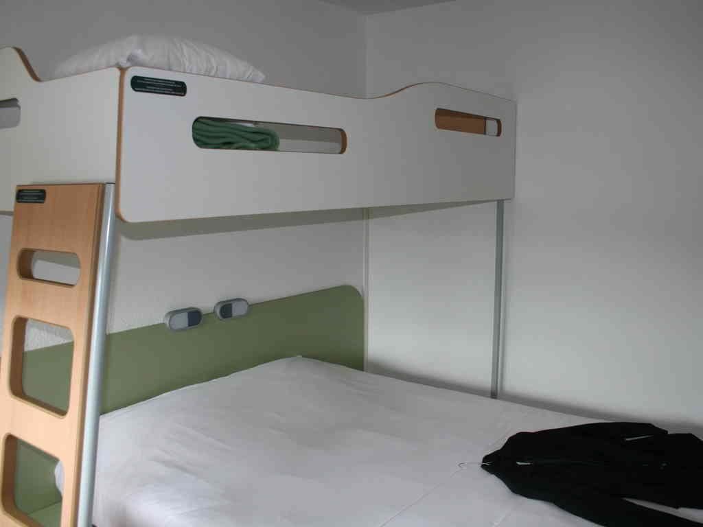Een stapelbed met een groen hoofdeinde, een witte matras en een zwart jack op het onderste bed.