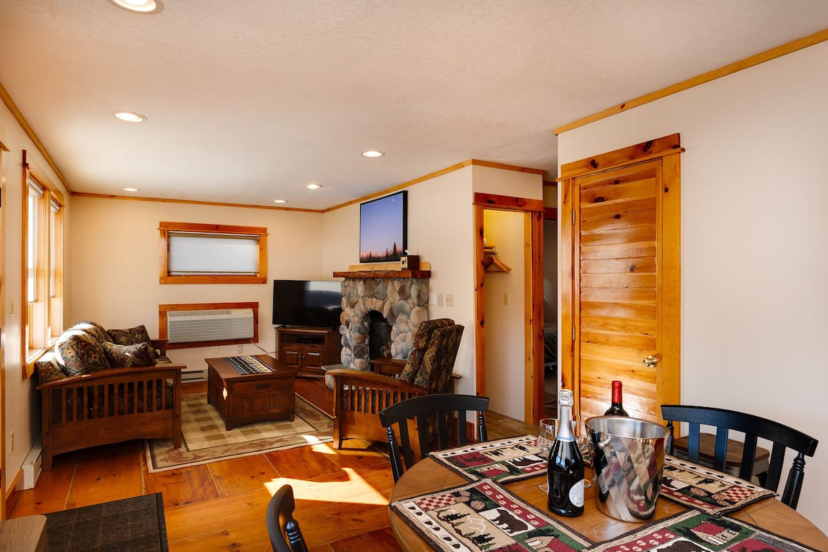 A cozy living room with a stone fireplace, wooden furniture, and a television.