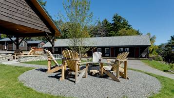 A wooden deck with Adirondack chairs and a table, surrounded by a gravel area with a building in the background.