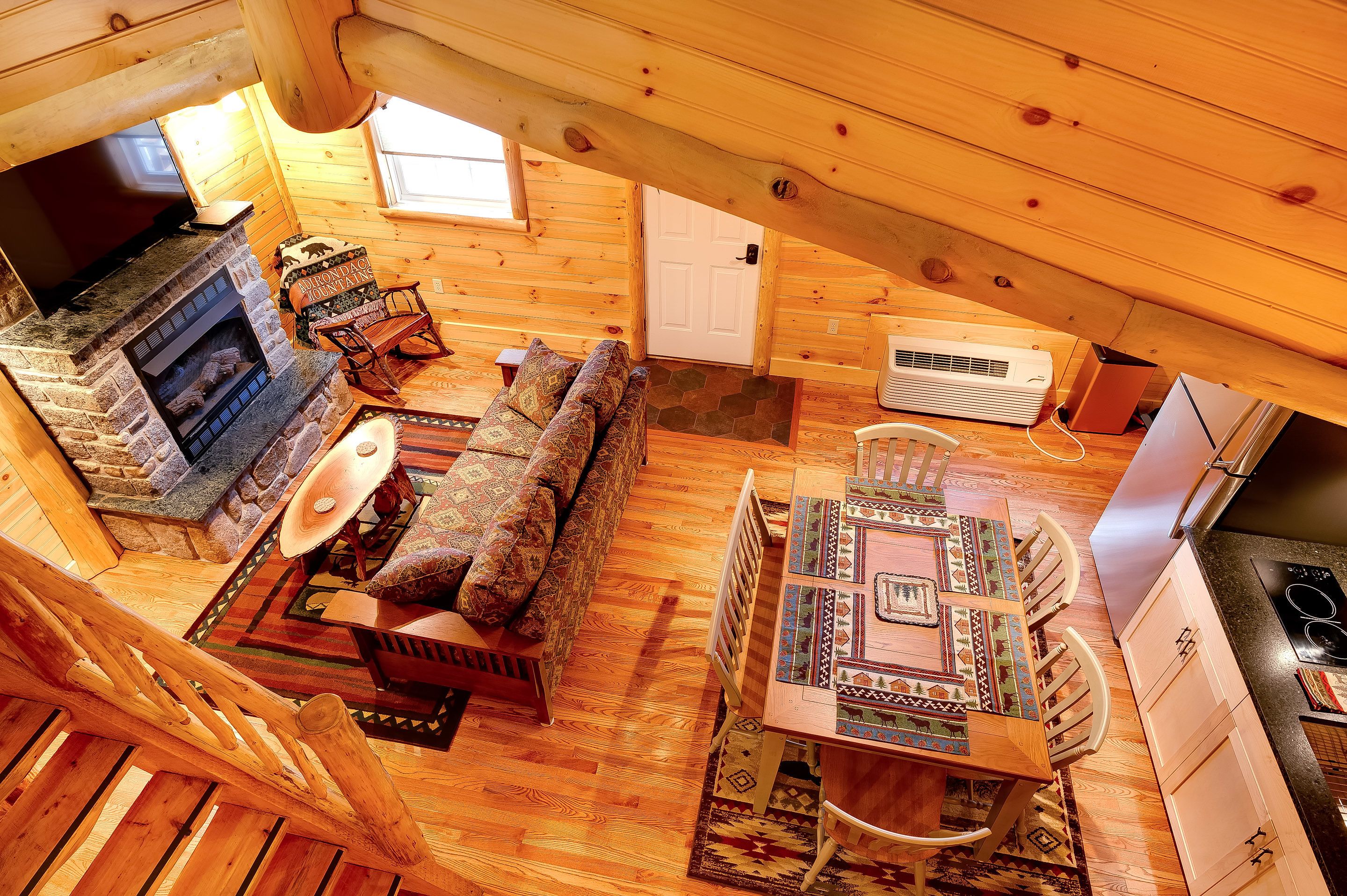 L’intérieur d’un chalet confortable, avec une cheminée en pierre, un canapé, une table à manger et un coin cuisine.
