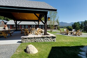 A covered outdoor seating area with stone walls and wooden furniture, overlooking a mountainous landscape. - Cobble Mountain Lodge (Lake Placid)