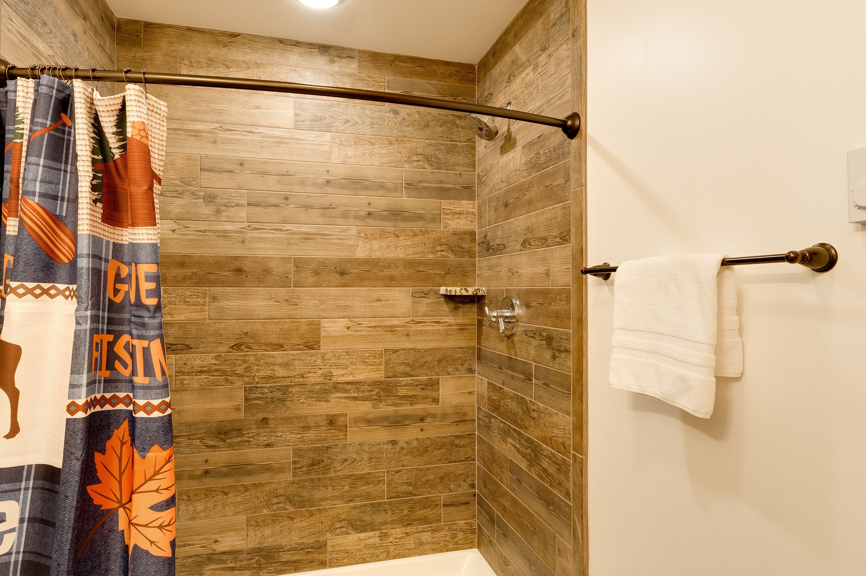 A shower with wooden paneling, a shower curtain with a leaf pattern, and a white towel on a towel rack.