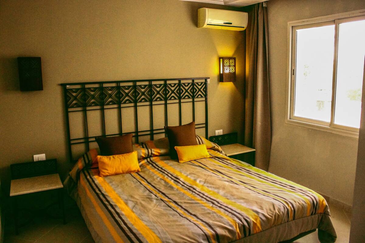 Una cama bien hecha con ropa de cama a rayas, un cabecero con estampado geométrico y una mesita de noche con una lámpara.