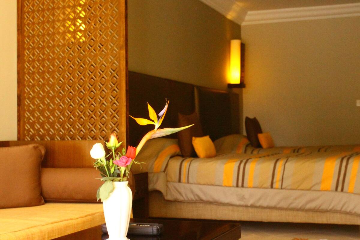 Una habitación de hotel con sofá, cama con ropa de cama a rayas y un florero con flores sobre una mesa.