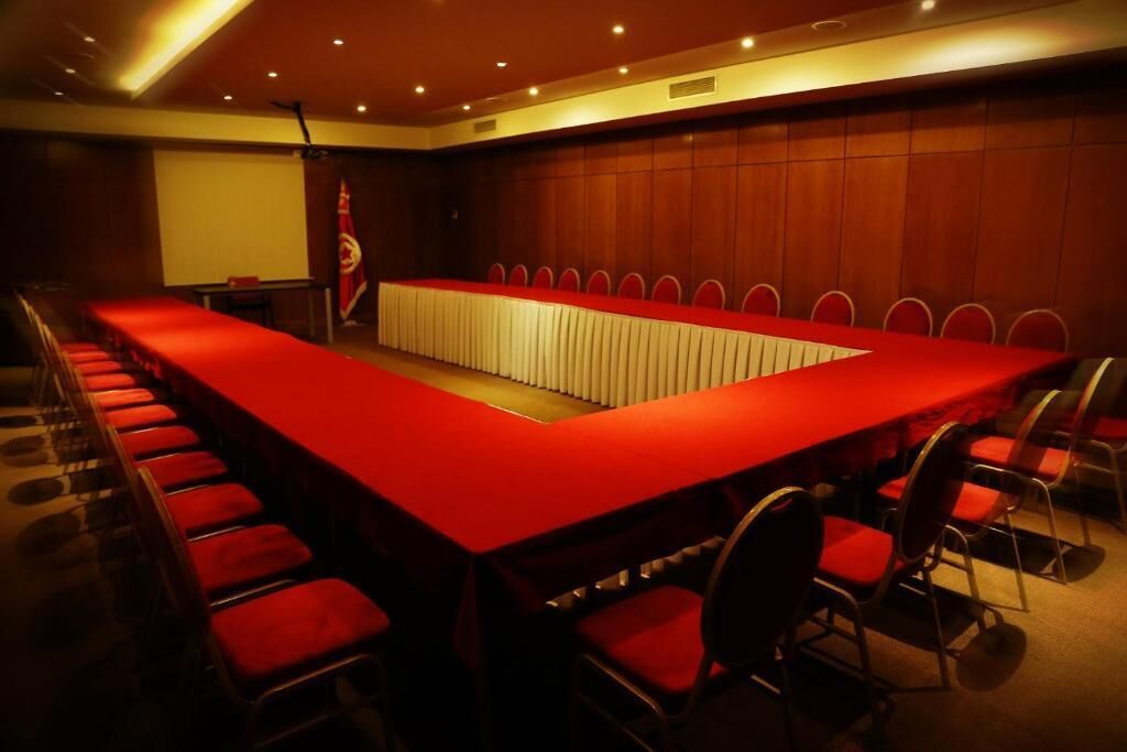 Un salón de conferencias con una larga mesa y sillas, un atril y una bandera.