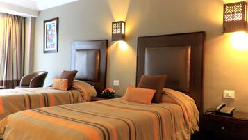 A hotel room with two beds, each with striped bedding and matching headboards. There are bedside tables with lamps and a telephone.