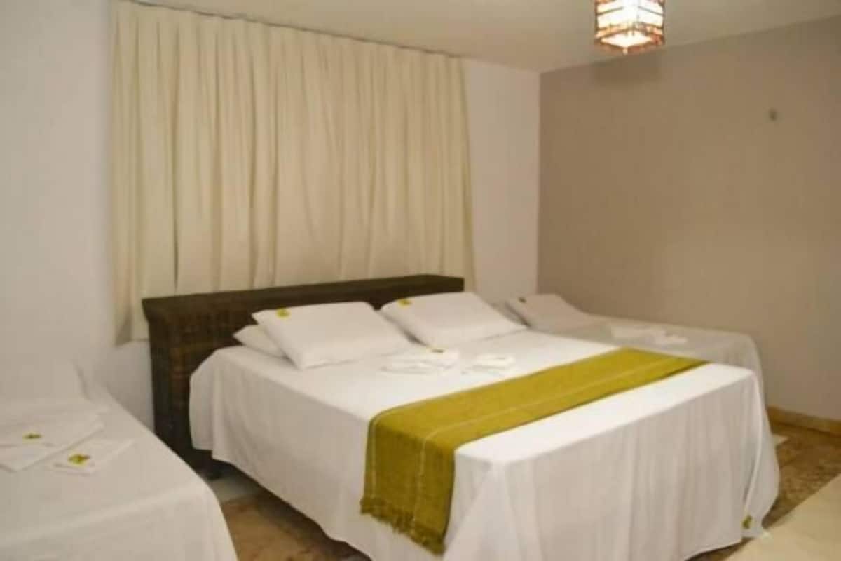 A hotel room with two single beds, a large bed, and a separate bed on the left.
