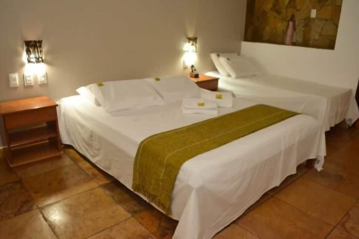 A hotel room with two beds, a nightstand, a wall-mounted lamp, and a painting.