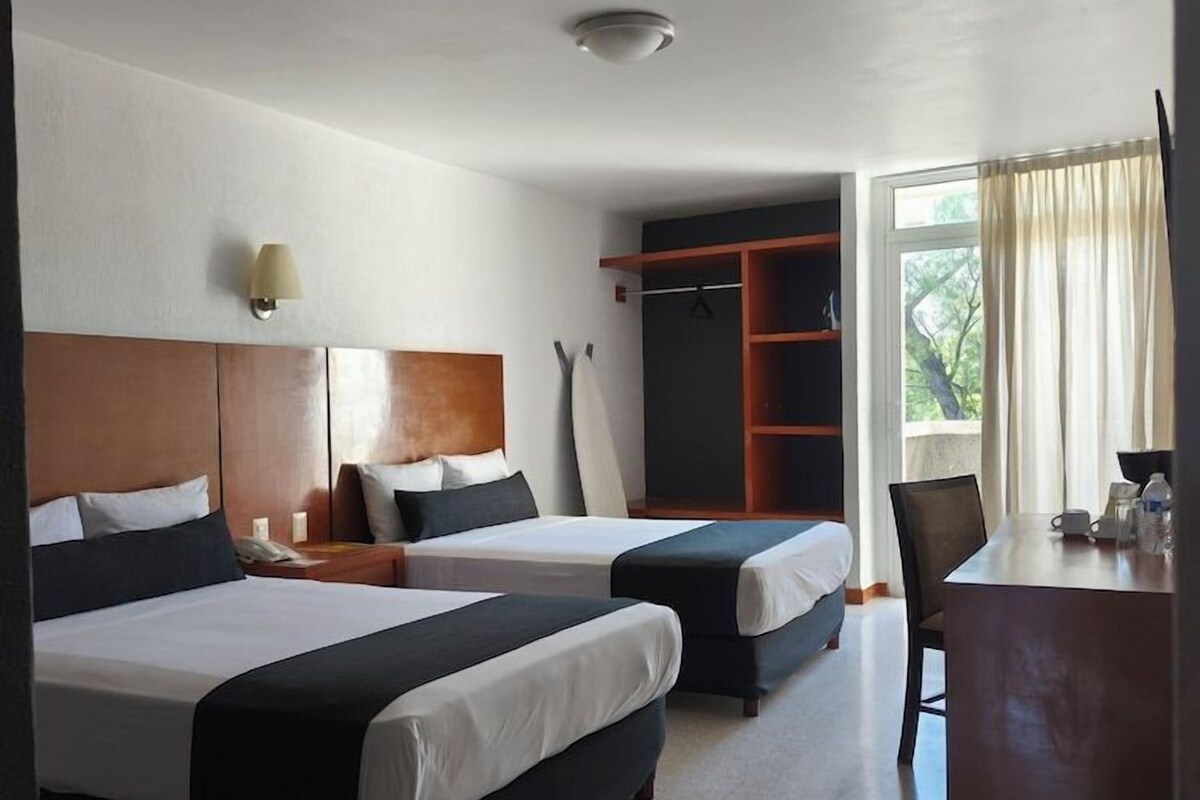 A hotel room with two beds, a desk, a chair, a wardrobe, and a window with curtains.