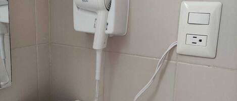 A bathroom with a white hairdryer mounted on the wall, a power outlet, and a towel with a logo.