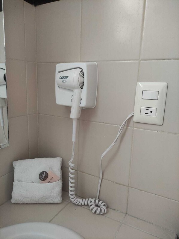 A bathroom with a white hairdryer mounted on the wall, a power outlet, and a towel with a logo. - Hotel Central Veracruz (Veracruz)