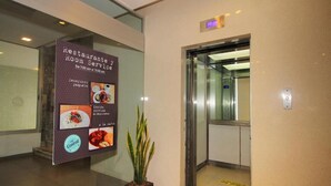 Un hall de hotel con restaurante, servicio de habitaciones, una planta en maceta y un ascensor.